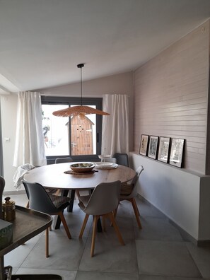 Ein Essbereich mit einem runden Tisch, Stühlen, einer Hängeleuchte, einem Fenster mit Vorhängen und gerahmten Bildern an der Wand.