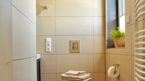 A small bathroom with a toilet, a stack of towels, a trash bin, and a wall-mounted mirror. - Cozy vacation home with 2 separate living units in the Thuringian Forest (Suhl)
