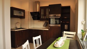 A modern kitchen with dark wooden cabinets, a stainless steel oven, and a dining area with a green tablecloth. - Cozy vacation home with 2 separate living units in the Thuringian Forest (Suhl)