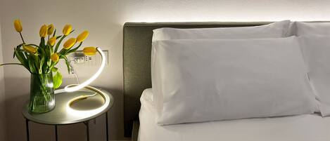 Een hotelkamer met een bed, een nachtkastje met een lamp, en een lijst met een abstract schilderij aan de muur.