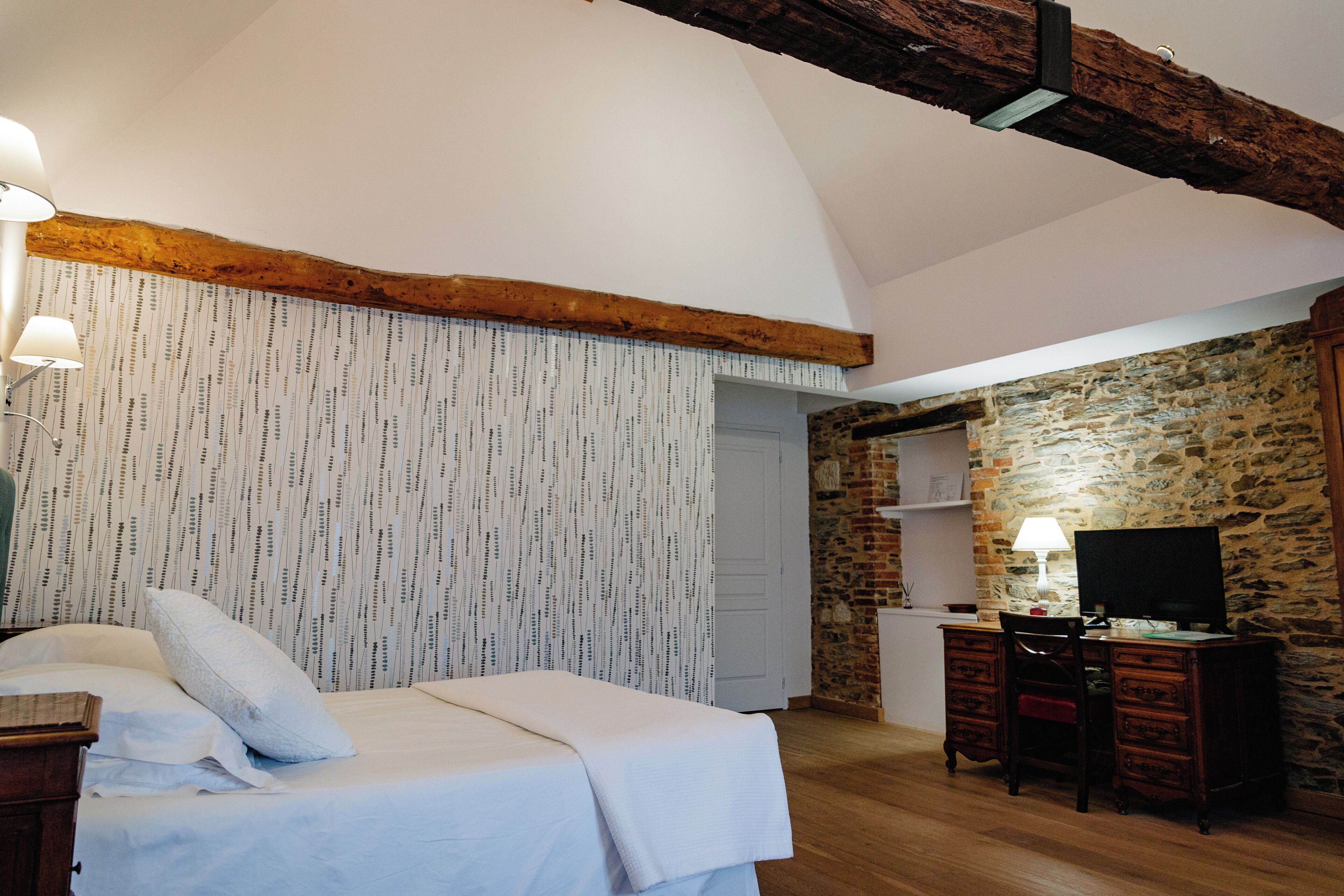 Een slaapkamer met een bed, een bureau met stoel, een televisie en een stenen muur.