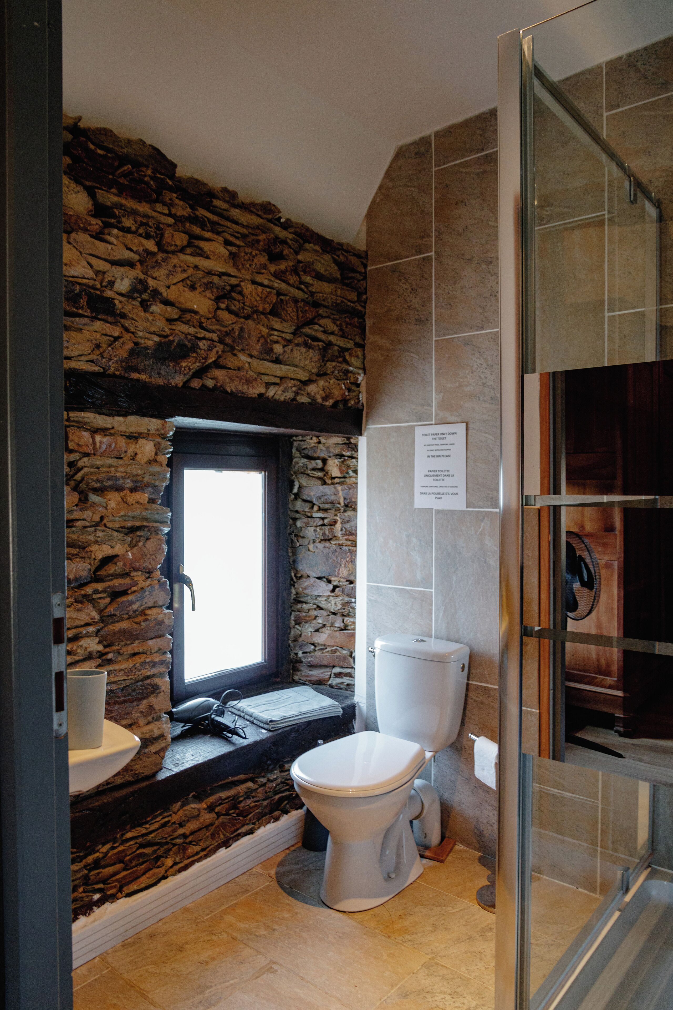 A bathroom with a stone wall, a window, a toilet, and a shower area.