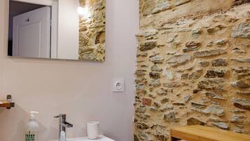 Un baño con pared de piedra, un lavabo blanco, un espejo y una estantería de madera.