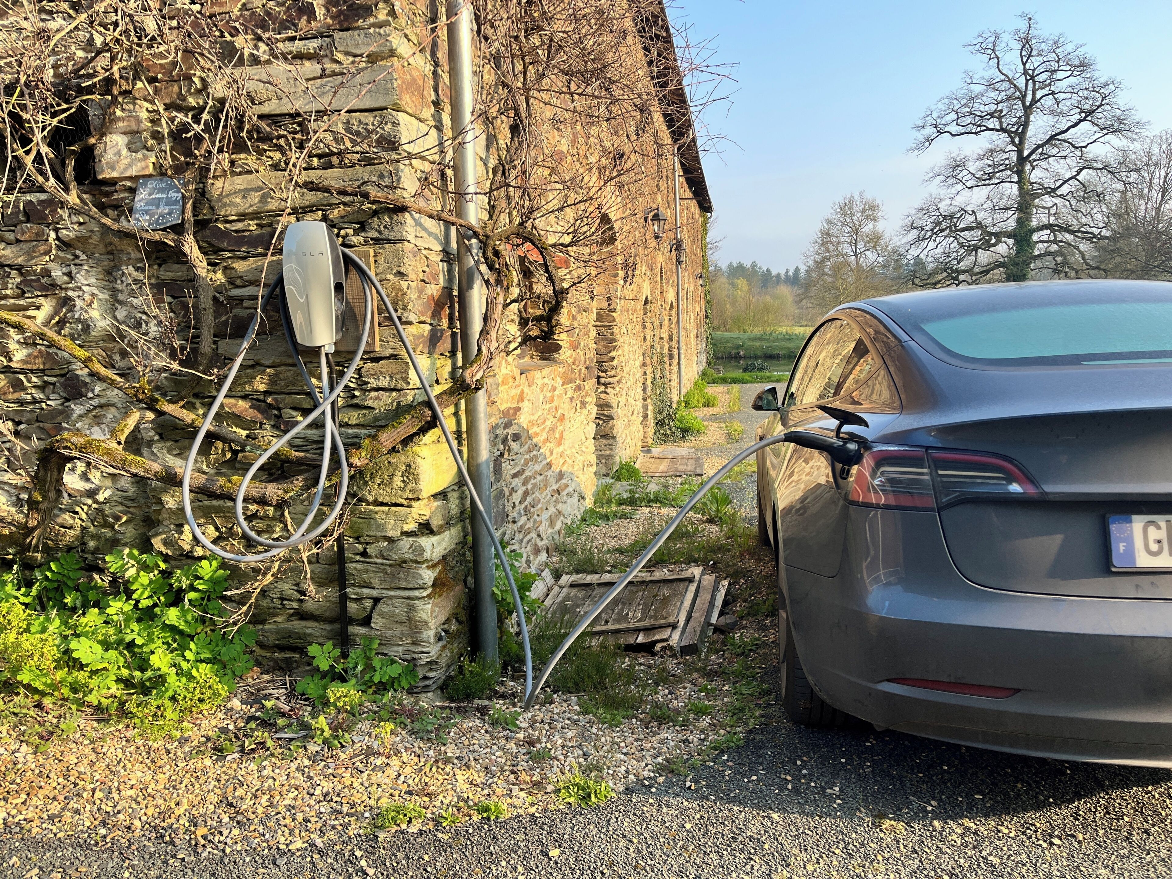 Une voiture est garée à côté d’un bâtiment en pierre, près d’une borne de recharge.