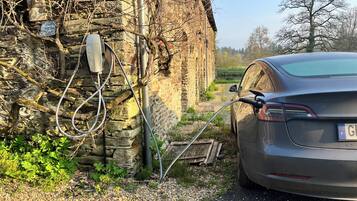 Une voiture est garée à côté d’un bâtiment en pierre, près d’une borne de recharge.