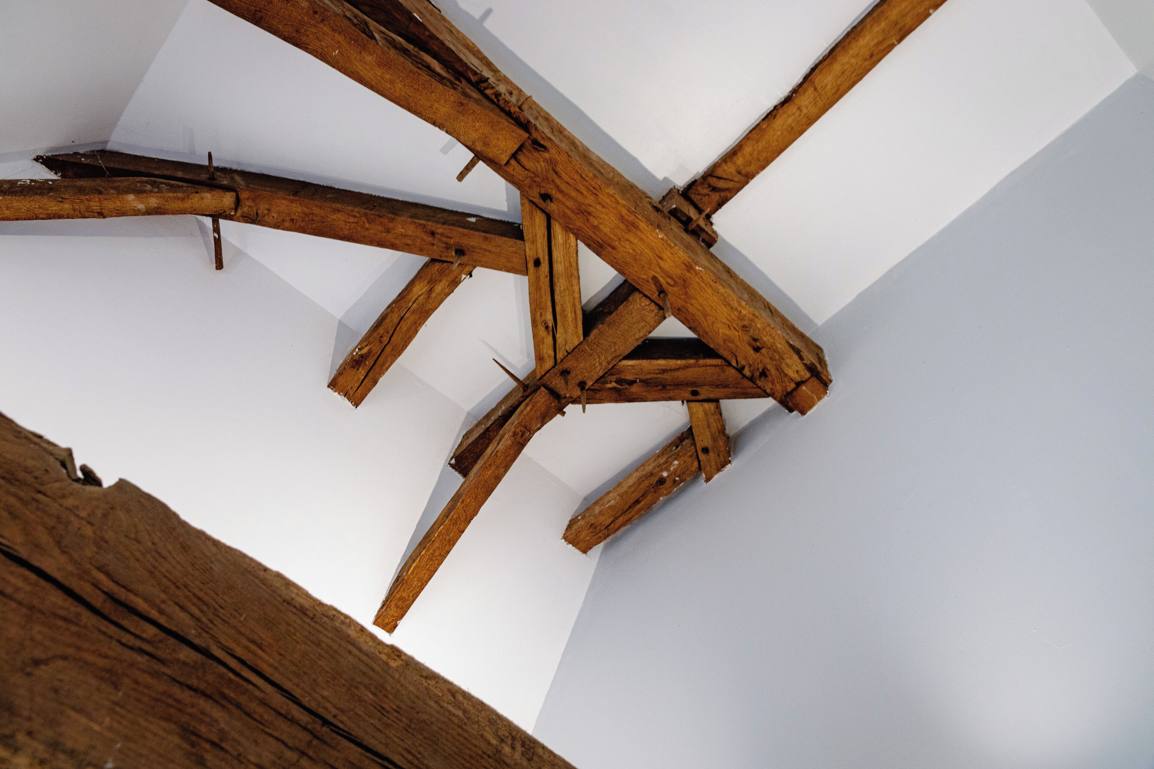 A wooden ceiling structure with beams and a white wall.