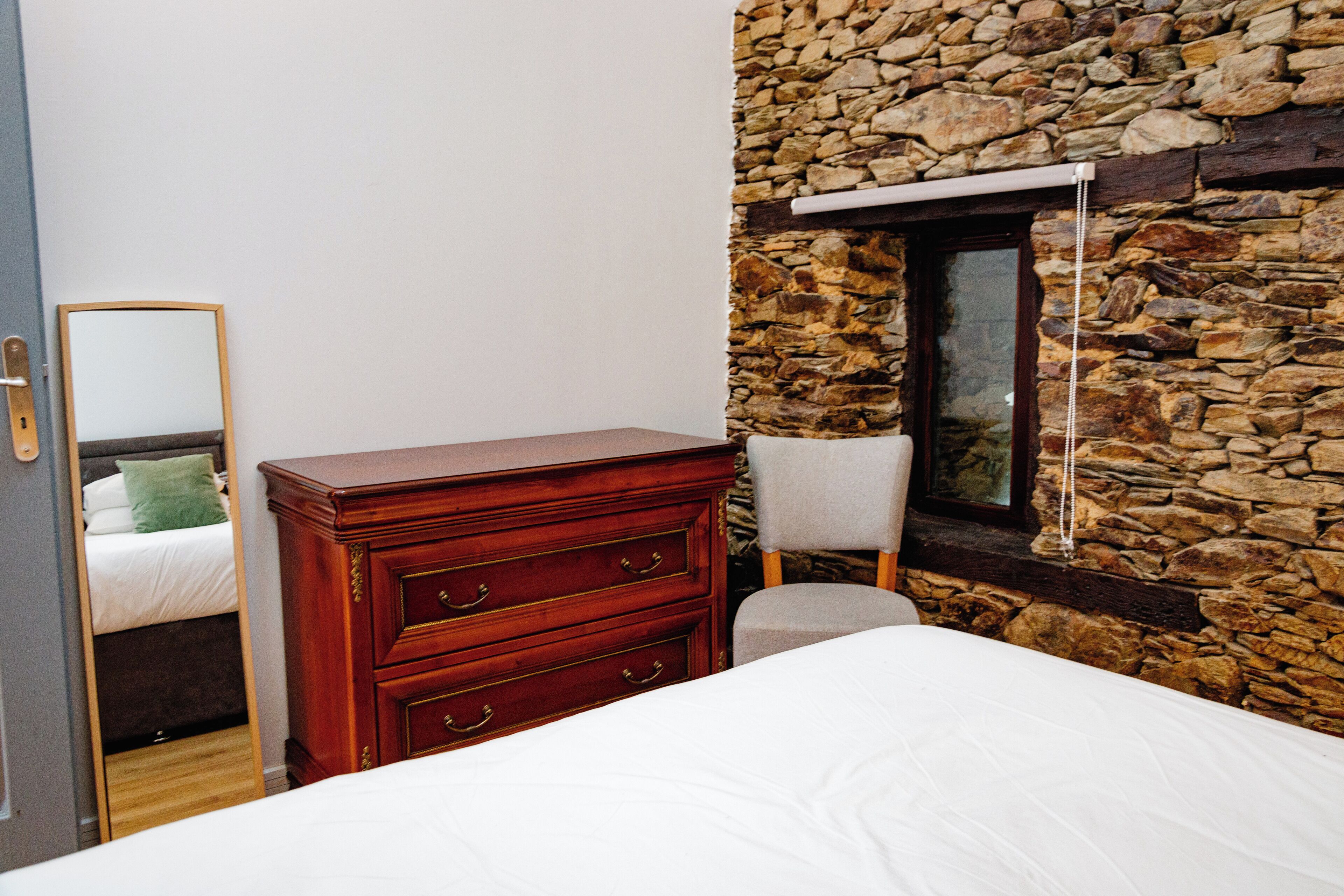 Ein Schlafzimmer mit einem Holzkoffer, einem Sessel, einem Bett und einer Steinwand.