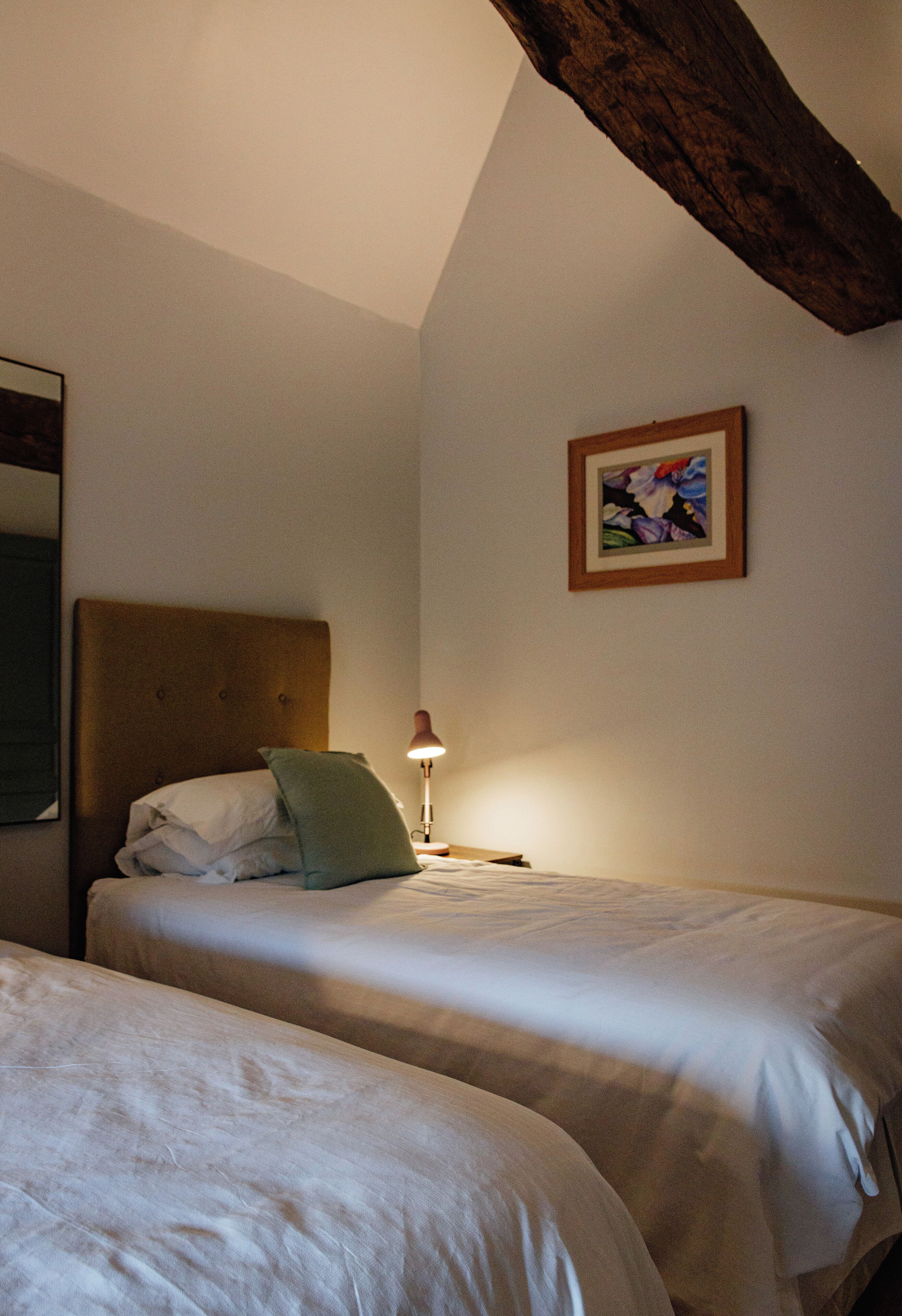 Ein Zimmer mit zwei Betten, einem Holzbalken an der Decke, einem Bild an der Wand und einer Nachttischlampe.