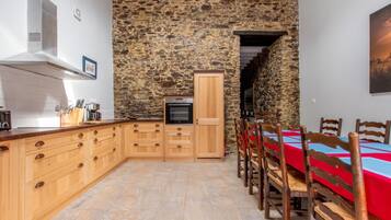 A kitchen with wooden cabinets, a stone wall, and a dining area with wooden chairs and a red tablecloth.