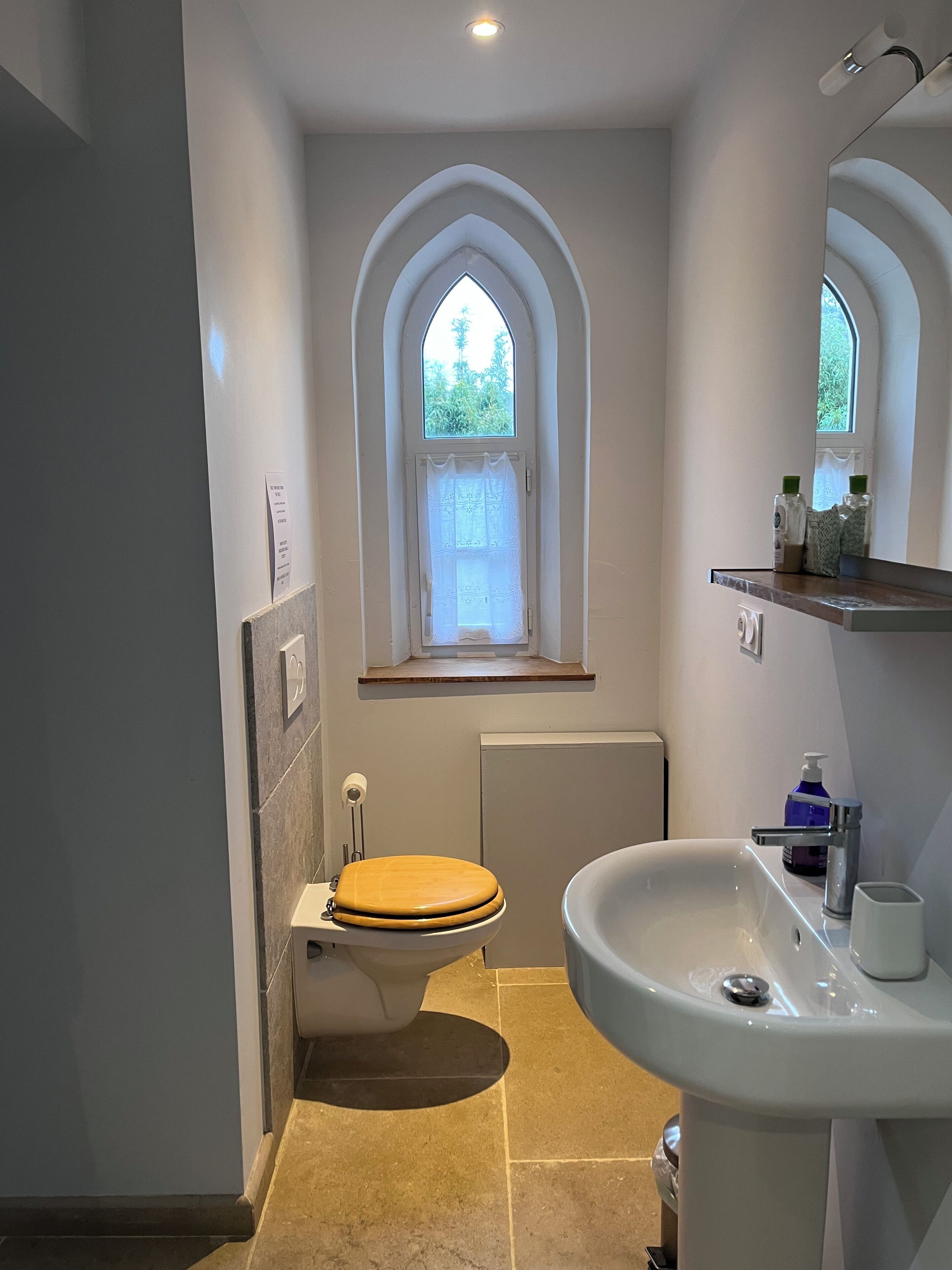 A bathroom with a toilet, sink, and window.