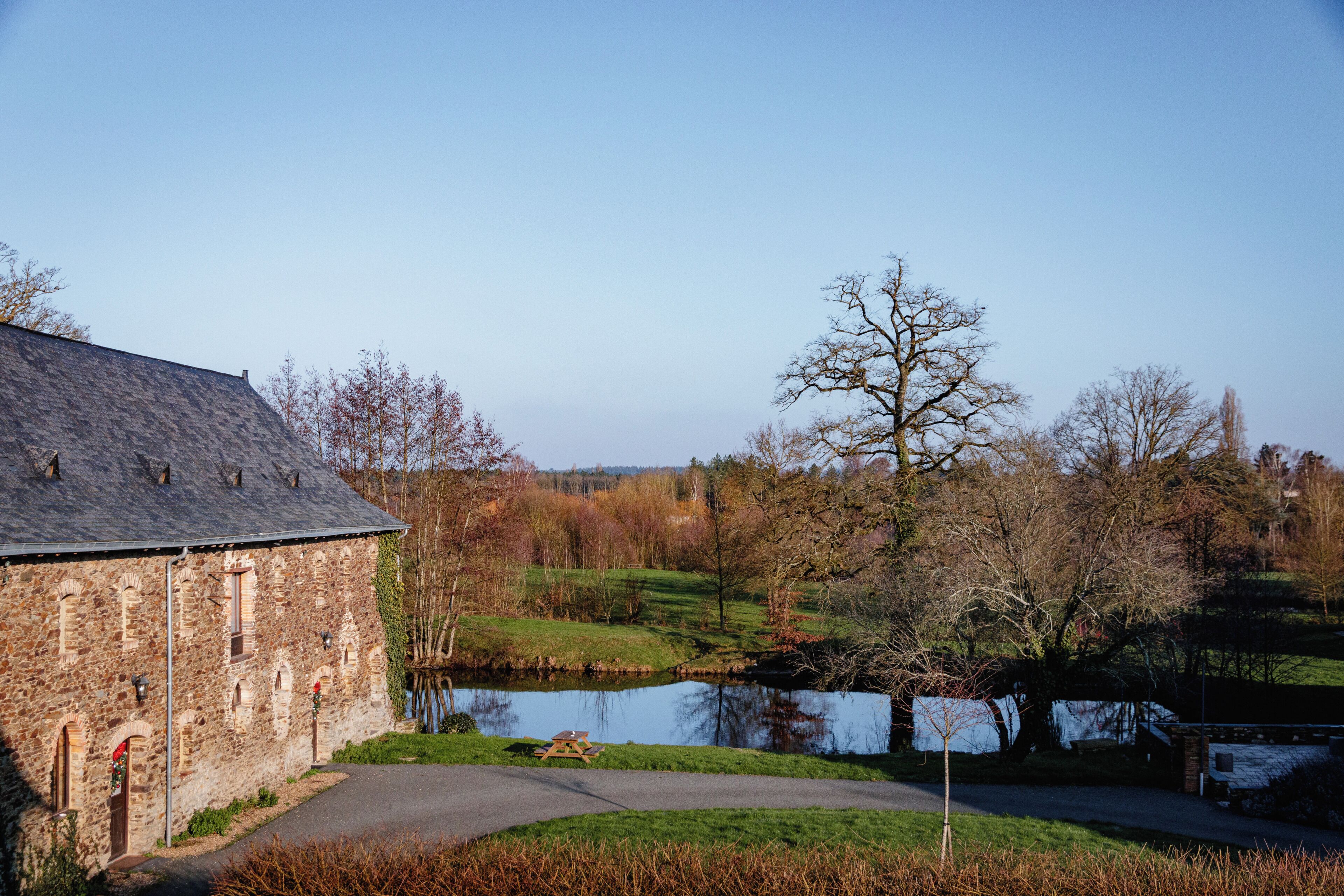 A stone building with a pond, trees, and a clear sky.