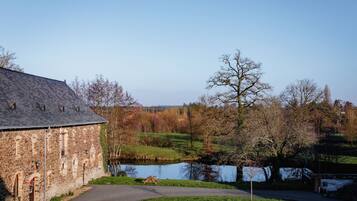 A stone building with a pond, trees, and a clear sky.