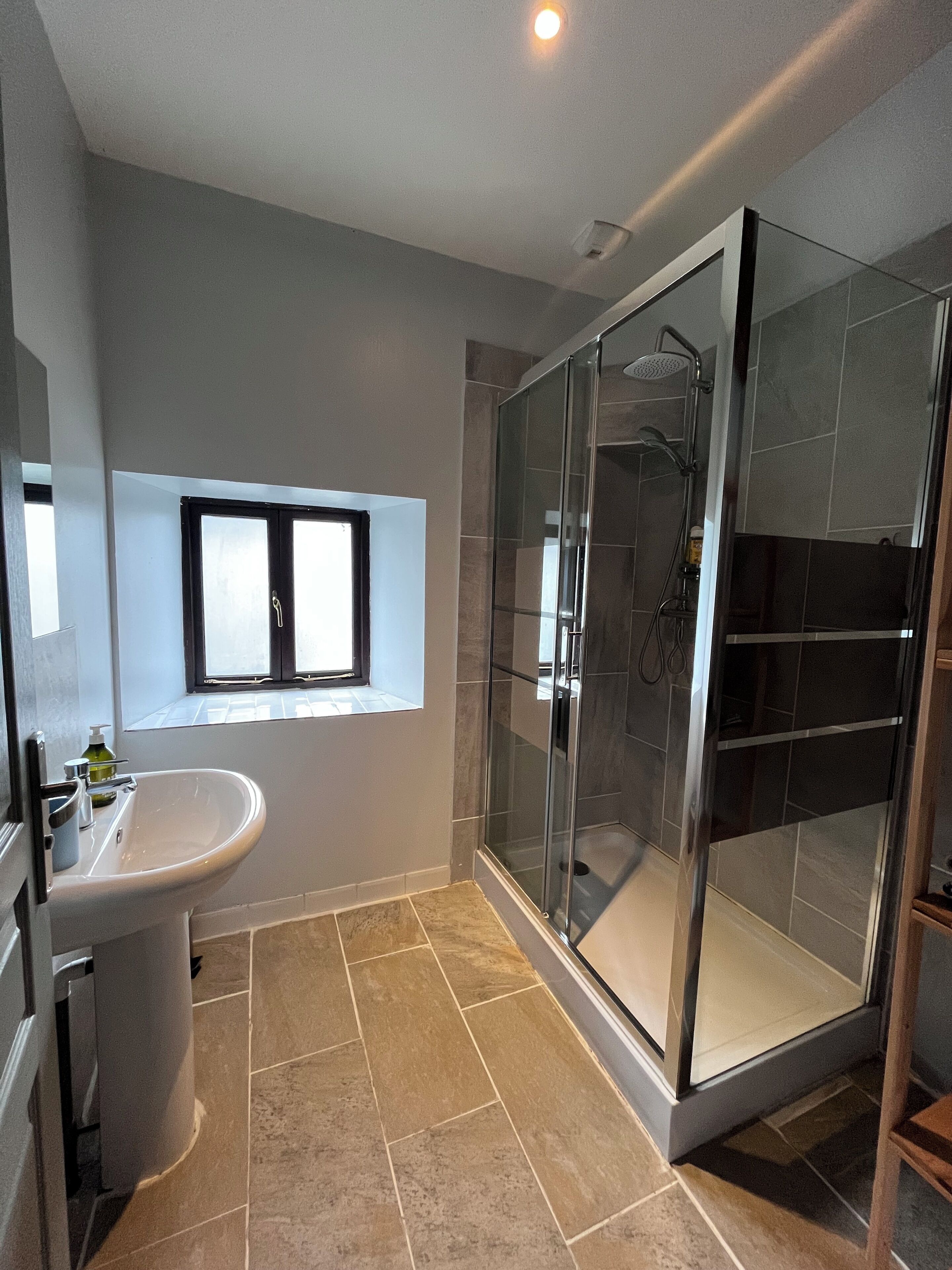 Une salle de bain moderne avec une douche à parois de verre, un lavabo et une fenêtre située au-dessus du miroir.