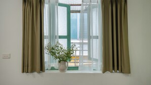 A window with beige curtains, a white vase with flowers, and a view of a wooden deck. - Quiet Family 6BR Home/Large Balcony/Street View/5' to Train St/Free Laundry (Hà Nội)
