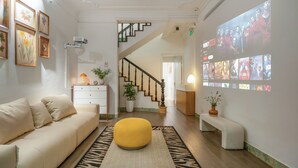 A modern living room with a sofa, ottoman, and a large screen displaying movie posters. - Quiet Family 6BR Home/Large Balcony/Street View/5' to Train St/Free Laundry (Hà Nội)