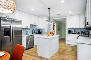 Eine moderne Küche mit weißen Schränken, einer zentralen Kochinsel, Edelstahlgeräten und einer Küchenrückwand mit Fischgrätenmuster.
