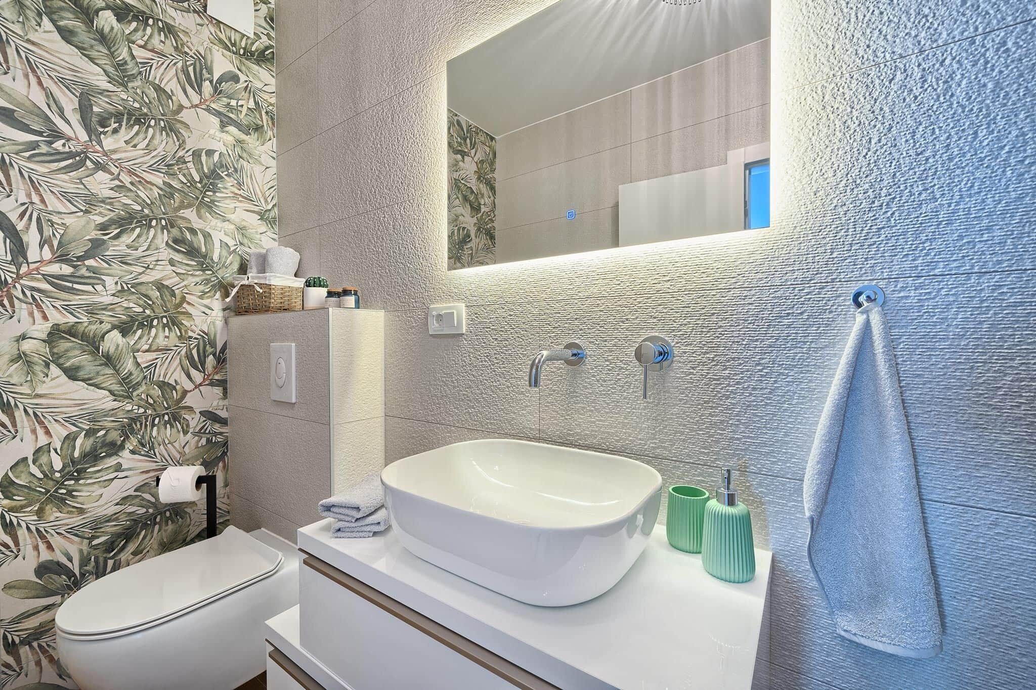 A modern bathroom with a white sink, a large mirror, and a textured wall.