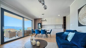 Un salon moderne avec un canapé bleu, une table basse ronde agrémentée d’objets décoratifs et un coin repas avec des chaises bleues.