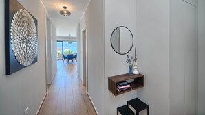 Un couloir moderne agrémenté d’une grande œuvre d’art abstraite murale, d’un miroir rond et d’une petite étagère en bois où sont posés des livres.