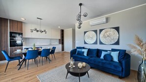 Un salon moderne avec un canapé bleu, un coin repas avec des chaises et une cuisine en arrière-plan.