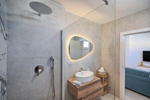 A modern bathroom with a shower, a round mirror, a wooden vanity, and a blue sofa in the adjacent room. - Mićo's Beach Studio With Pool (Slatine)