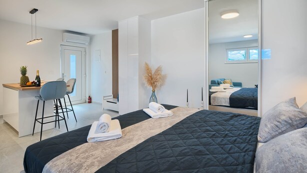 Ett modernt hotellrum med en stor säng, ett skrivbord med en stol, en minibar och en stor spegel.