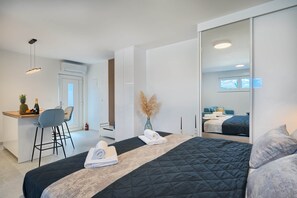 A modern hotel room with a large bed, a desk with a chair, a minibar, and a large mirror. - Mićo's Beach Studio With Pool (Slatine)