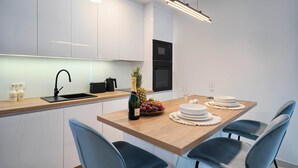 Ett modernt kök med vita skåp, en bänkskiva i trä, en diskho, en mikrovågsugn och en matplats med ett träbord där det är dukat för två personer.