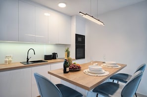 A modern kitchen with white cabinets, a wooden countertop, a sink, a microwave, and a dining area with a wooden table set for two.