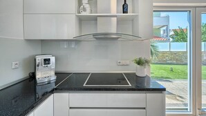 Eine moderne Küche mit integrierter Espressomaschine, einer Glaskochplatte und Blick ins Freie.