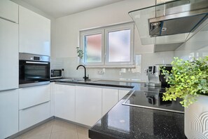 Een moderne keuken met witte kasten, een zwart aanrecht, een ingebouwde oven, een magnetron en een raam met geëtste glas.