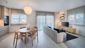 Een moderne woonkamer met een eethoek, een bank, een televisie en een groot raam.
