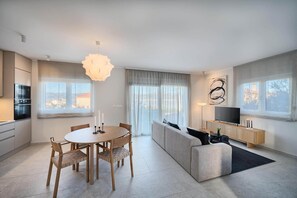 A modern living room with a dining area, a sofa, a TV, and a large window. - Tina's Tiny Beach House (Slatine)