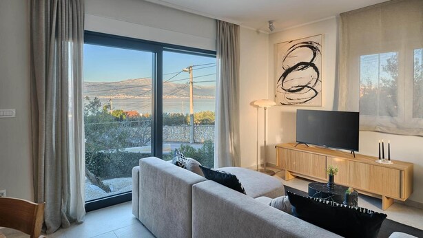 Een moderne woonkamer met een grote schuifpui, een flatscreen televisie op een houten console, en een minimalistische inrichting.