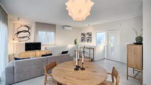 Een moderne woonkamer met een ronde houten tafel, een grijze bank en een televisie op een houten kast.
