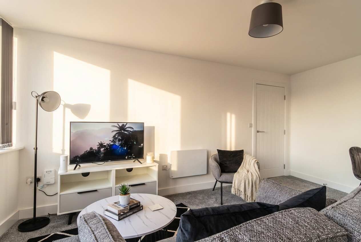Una sala de estar moderna con una televisión de pantalla plana, una mesa de centro redonda, un sofá, una lámpara de pie y una puerta.