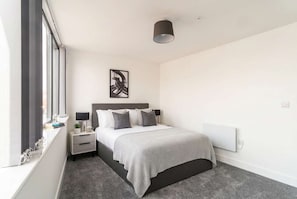 A bedroom with a bed, bedside tables, a lamp, a window, and a radiator. - Modern & Bright 1 Bed Apartment in Central Wrexham (Wrexham)