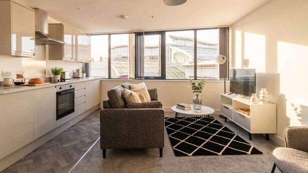 Ein zeitgemäßer Wohnraum mit einer Küche, einem Sofa, einem Couchtisch und einem Fernseher.