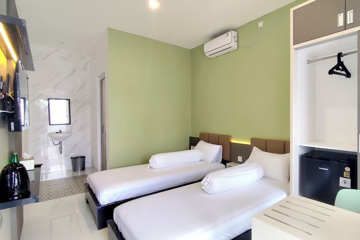 Une chambre d’hôtel avec deux lits, un bureau, un miroir, un lavabo et un appareil de climatisation.