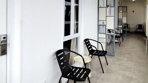 Un couloir aux murs blancs, aux chaises noires et au sol carrelé.