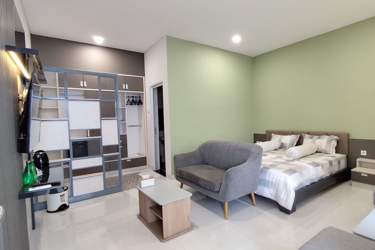 Une chambre à coucher moderne avec un lit, un fauteuil gris, une petite table, une armoire et un mur vert.