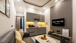 A modern living room with a sofa, coffee table, and a flat-screen TV mounted on a wall. - Saltstayz Premier Near Sector 44 Corporate Hub (Gurugram)
