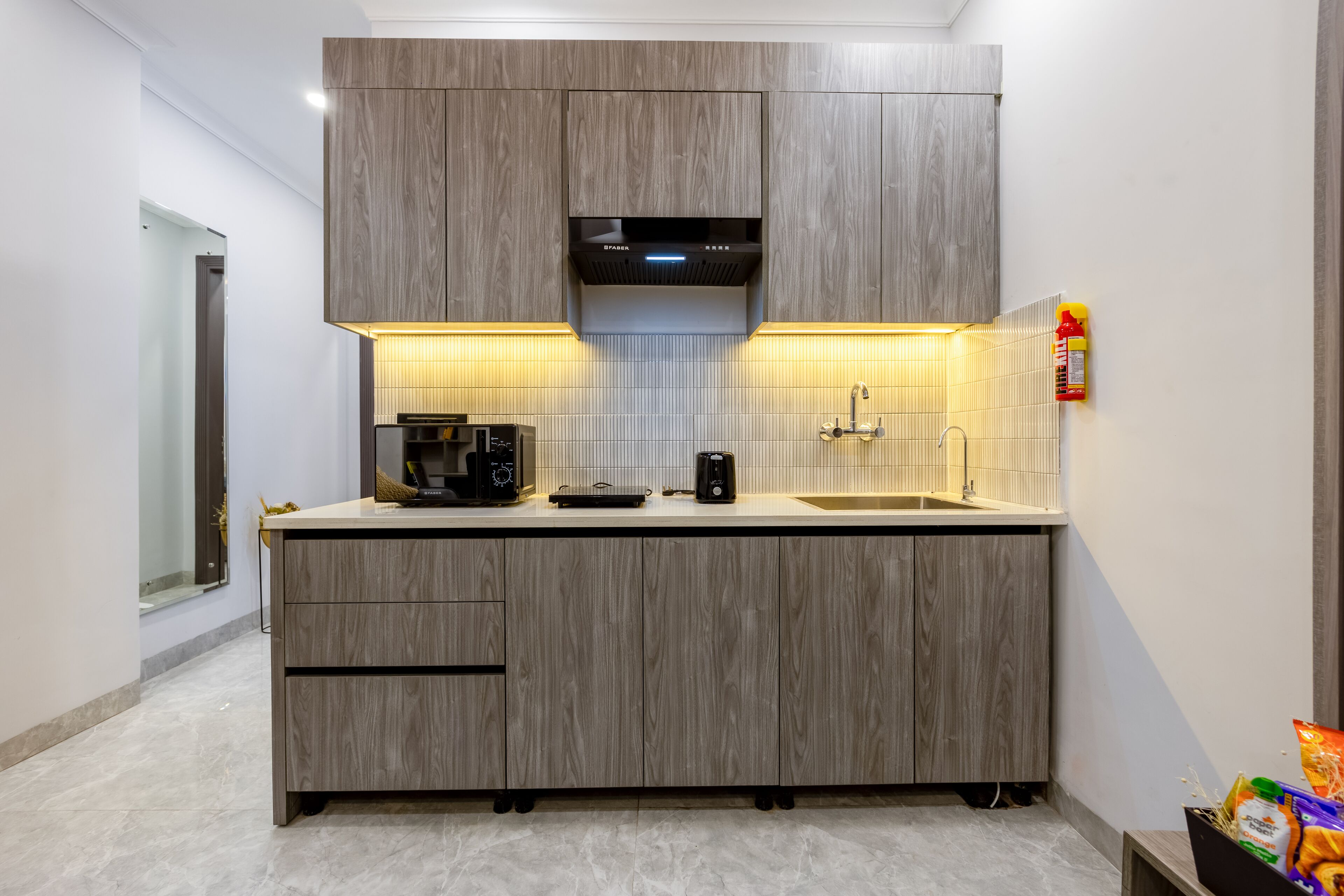 A compact kitchen with wood cabinetry, a built-in range hood, a coffee maker, and a sink.