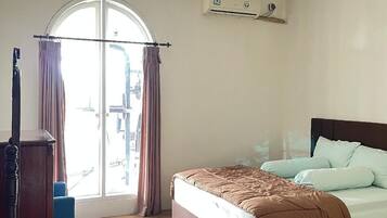 A bedroom with a bed, a window with curtains, a ceiling fan, and an air conditioning unit.
