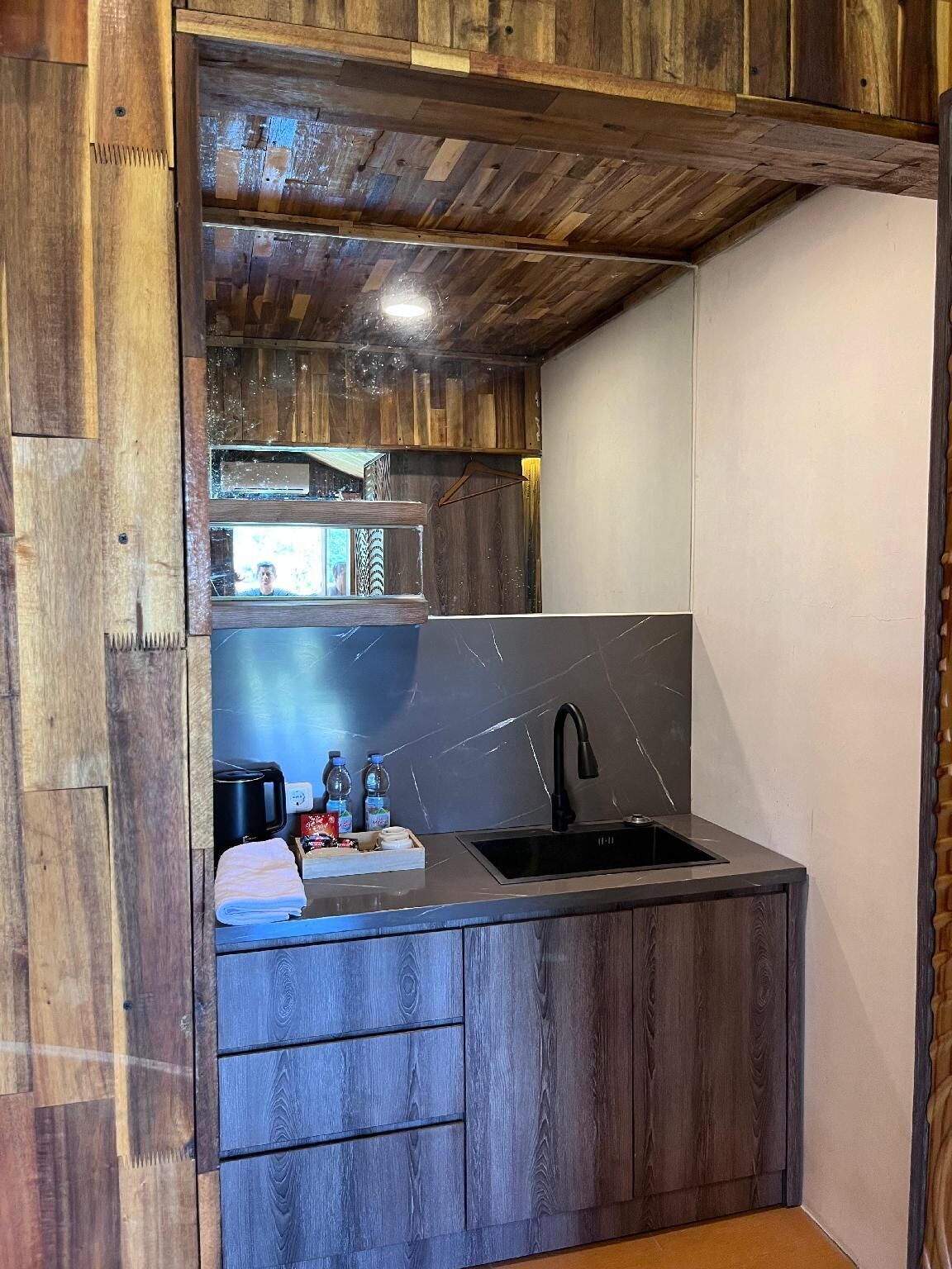 A compact kitchen with a wooden ceiling, a black sink, and a microwave.