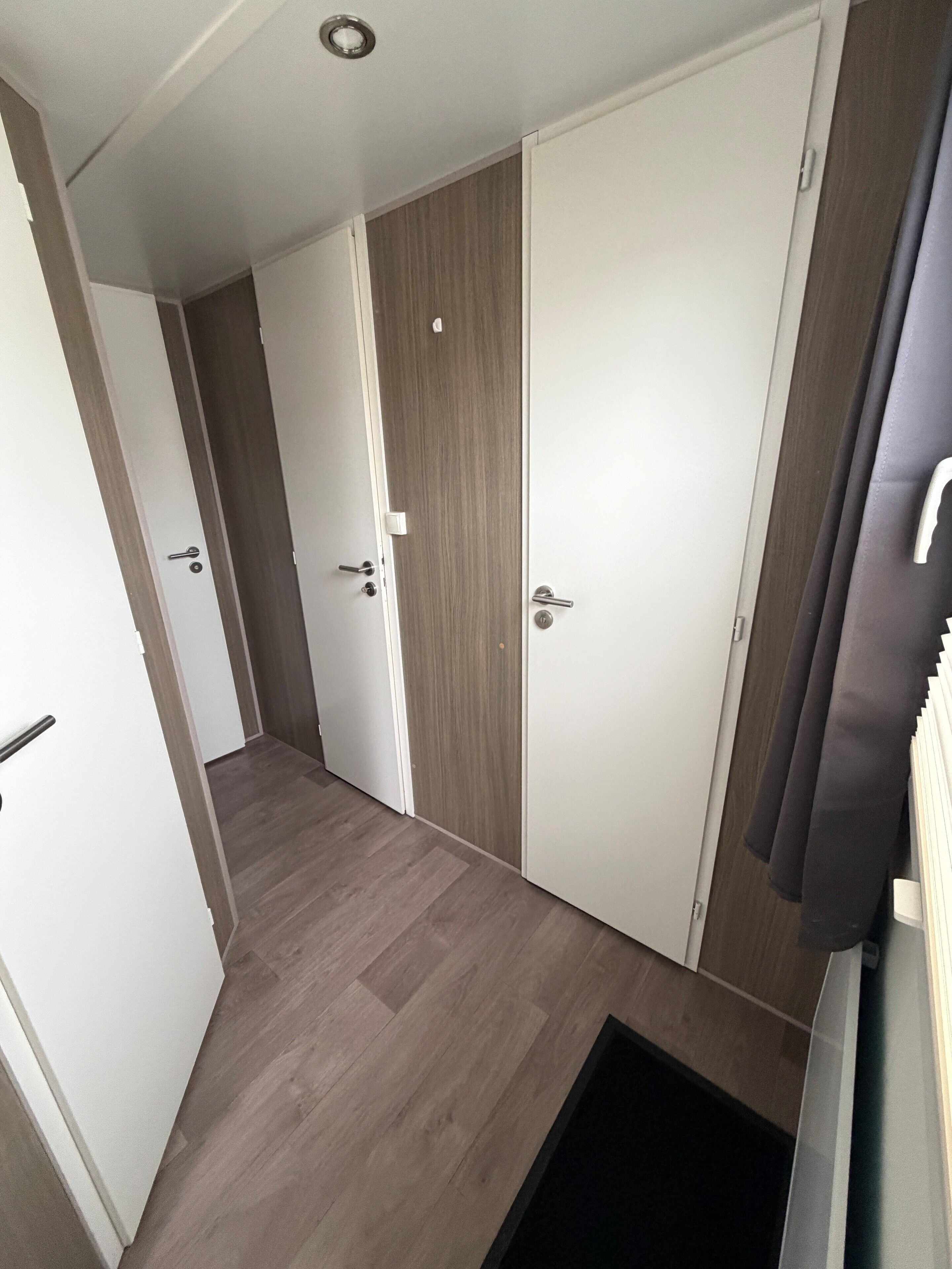 Un pasillo con suelo de madera, puertas blancas y un tapete negro en la entrada.