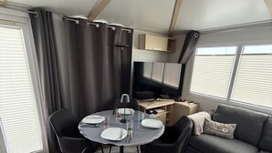 Una sala de estar moderna con una mesa de comedor redonda, sillas negras, un sofá gris y un televisor.