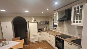 A modern kitchen with white cabinets, a wooden dining table, and a patterned rug.