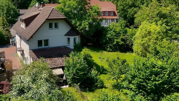 A two-story house with a sloped roof, surrounded by lush greenery and trees.