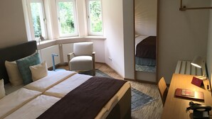 A bedroom with a bed, a chair, a desk, and a mirror.